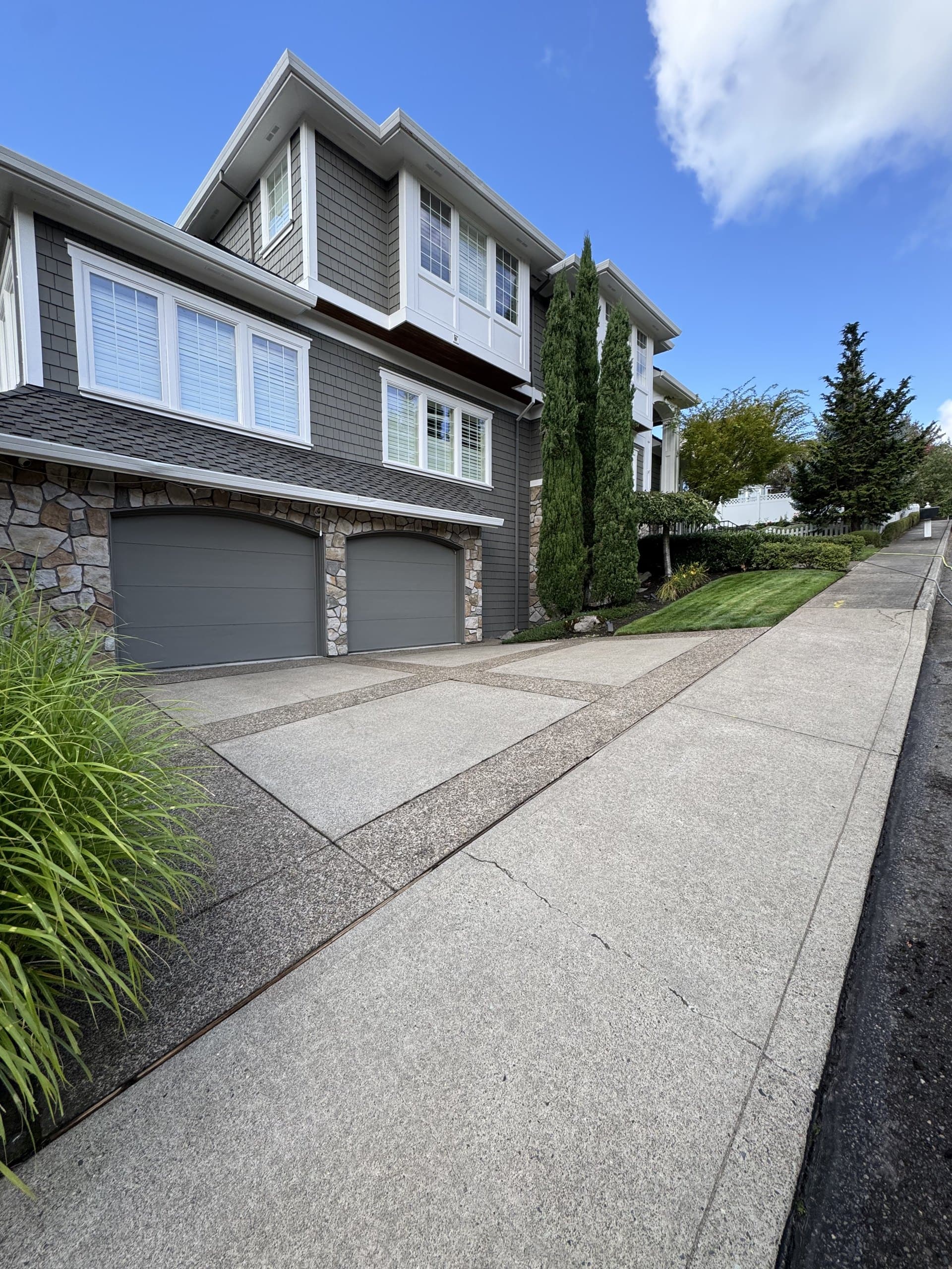 Freshly cleaned exposed-aggregate driveway and sidewalk in front of a two-story home.